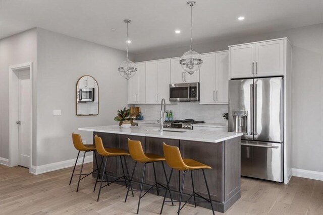 kitchen featuring decorative light fixtures, light hardwood / wood-style floors, tasteful backsplash, a kitchen island with sink, and appliances with stainless steel finishes