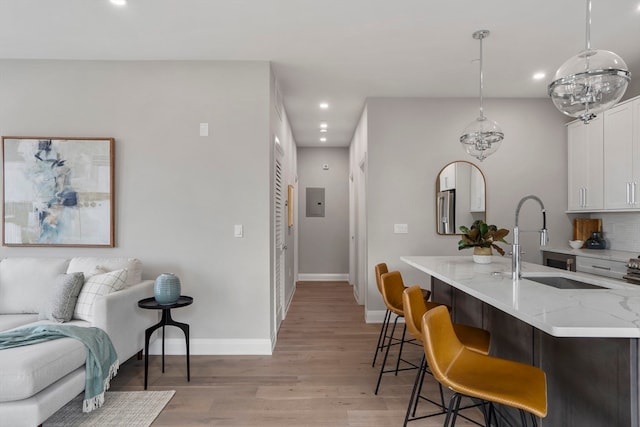 kitchen with light stone counters, light hardwood / wood-style flooring, a kitchen bar, white cabinetry, and sink