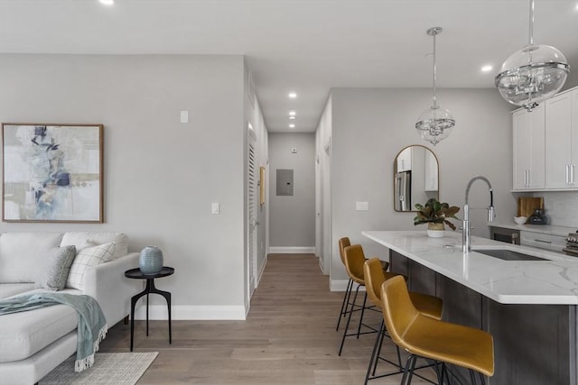 kitchen with decorative light fixtures, white cabinetry, sink, light stone countertops, and light wood-type flooring