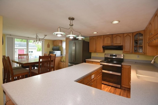 kitchen with appliances with stainless steel finishes, a sink, under cabinet range hood, glass insert cabinets, and light countertops