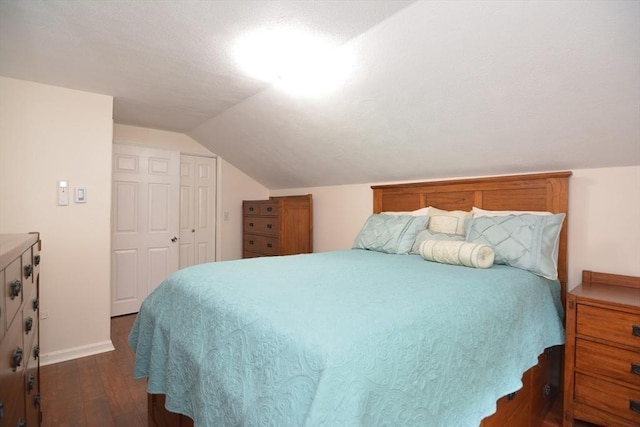 bedroom with dark wood-style flooring, vaulted ceiling, baseboards, and a closet