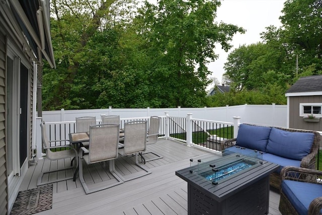 wooden terrace featuring outdoor dining space, a fenced backyard, an outdoor living space with a fire pit, an outbuilding, and a shed