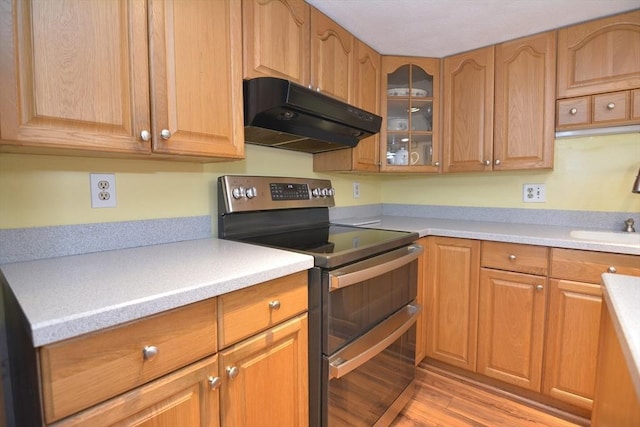 kitchen with double oven range, under cabinet range hood, light wood-type flooring, light countertops, and glass insert cabinets