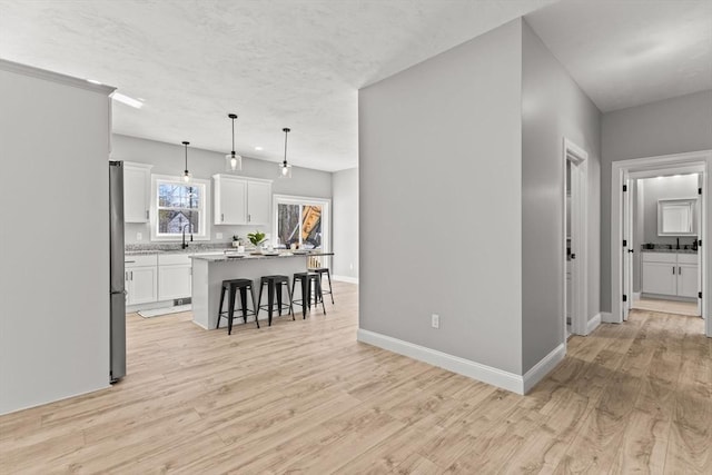 kitchen with white cabinetry, light hardwood / wood-style flooring, decorative light fixtures, a kitchen island, and a kitchen breakfast bar