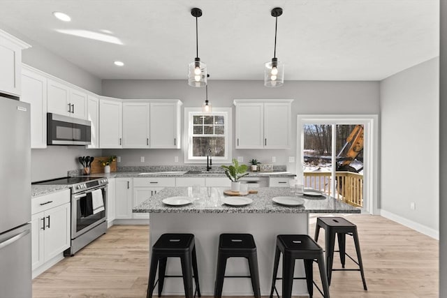 kitchen with appliances with stainless steel finishes, sink, light stone counters, white cabinetry, and a kitchen island