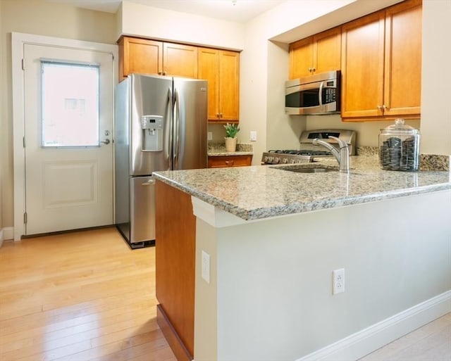 kitchen with kitchen peninsula, stainless steel appliances, light stone countertops, and sink