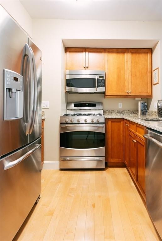 kitchen with appliances with stainless steel finishes, light hardwood / wood-style floors, sink, and light stone countertops