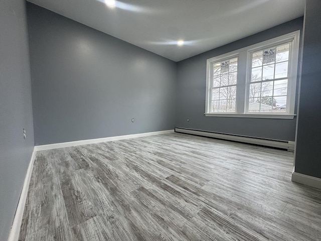 unfurnished room with baseboards, a baseboard heating unit, and wood finished floors