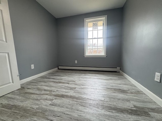 spare room with baseboards, a baseboard heating unit, and wood finished floors