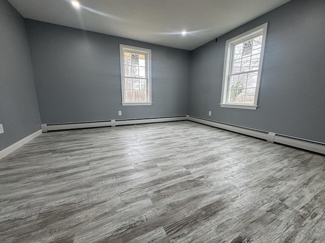 unfurnished room with a baseboard radiator, plenty of natural light, baseboards, and wood finished floors