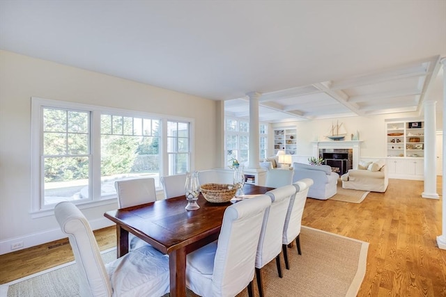 dining room featuring coffered ceiling, light wood-type flooring, a tile fireplace, and ornate columns