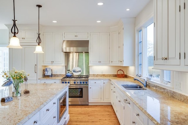 kitchen featuring sink, appliances with stainless steel finishes, white cabinets, decorative light fixtures, and wall chimney exhaust hood