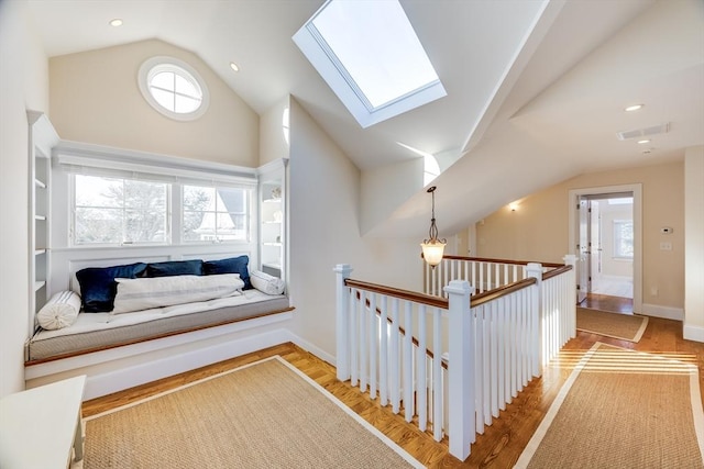 hall featuring high vaulted ceiling, light wood-type flooring, and a skylight