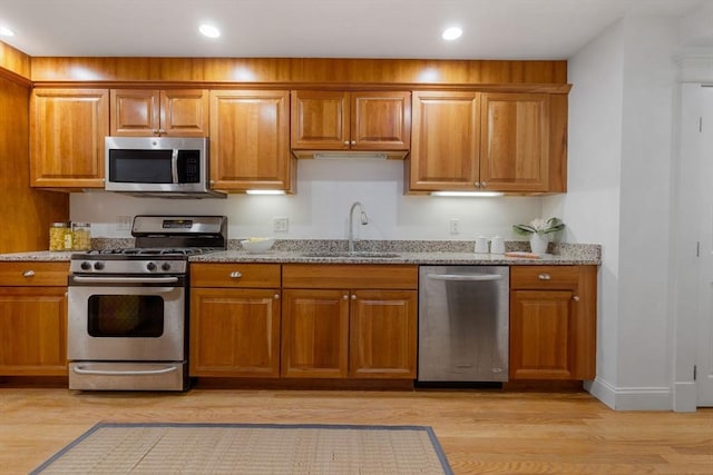 kitchen featuring stainless steel appliances, light stone countertops, sink, and light hardwood / wood-style flooring