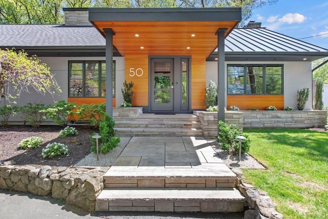 entrance to property featuring a standing seam roof, stucco siding, a chimney, and metal roof