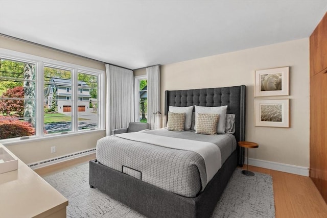 bedroom with a baseboard radiator, light wood-style floors, and baseboards