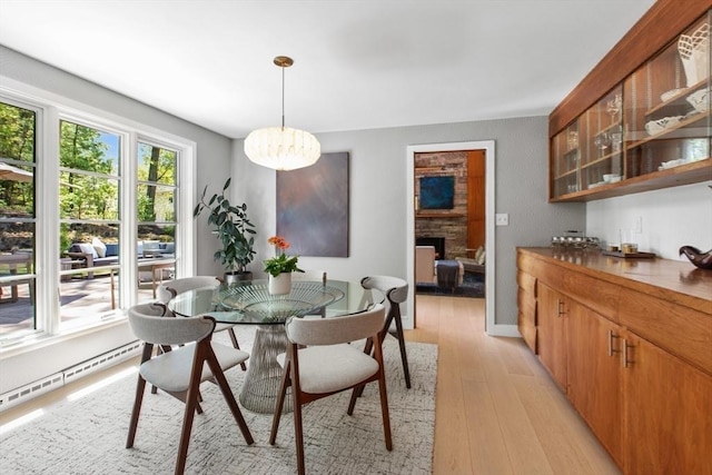 dining area featuring light wood-style flooring, a chandelier, a fireplace, a baseboard radiator, and baseboards