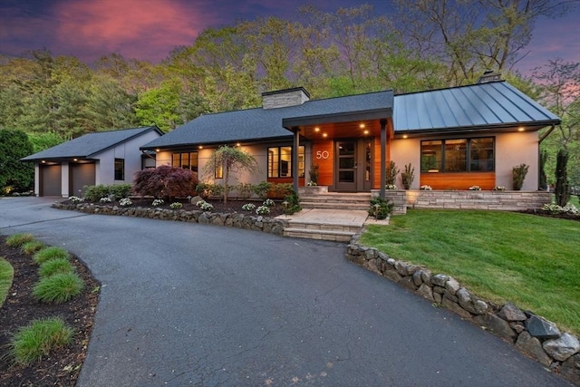 view of front of property featuring a chimney, a standing seam roof, a front lawn, metal roof, and stucco siding