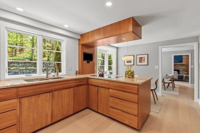 kitchen featuring a sink, a peninsula, light wood-style flooring, a stone fireplace, and light stone counters