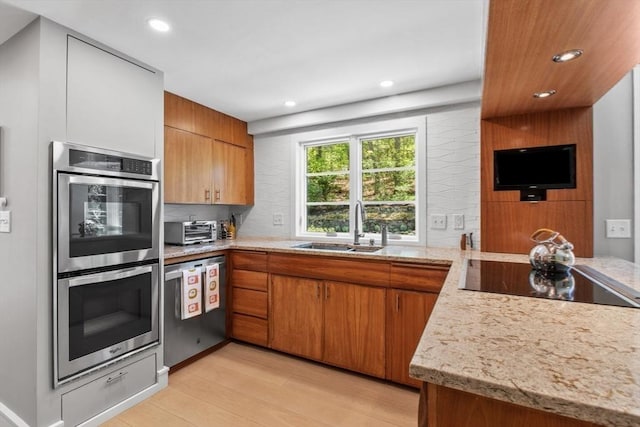 kitchen featuring stainless steel appliances, a sink, brown cabinetry, light wood finished floors, and recessed lighting