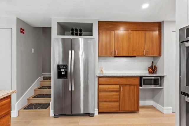 kitchen with appliances with stainless steel finishes, brown cabinets, light wood-style floors, and baseboards
