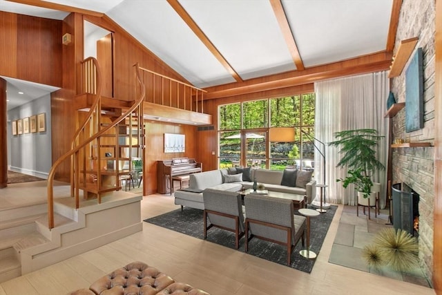 living room featuring stairway, wooden walls, wood finished floors, high vaulted ceiling, and a stone fireplace