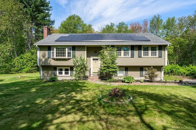bi-level home featuring a chimney, solar panels, entry steps, a front yard, and a shingled roof