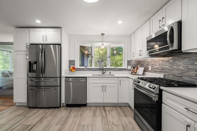 kitchen with stainless steel appliances, light countertops, decorative backsplash, white cabinetry, and a sink