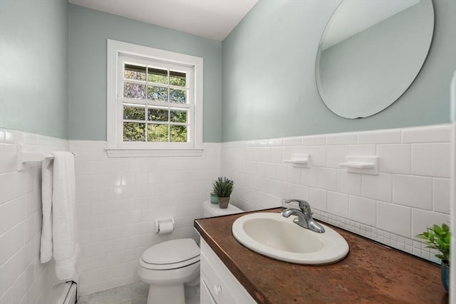 half bathroom with tile walls, toilet, a wainscoted wall, vanity, and baseboard heating