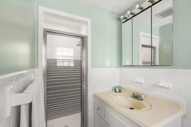 full bath with tile walls, a shower stall, wainscoting, and vanity