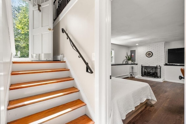 stairway with healthy amount of natural light, wood finished floors, and a fireplace