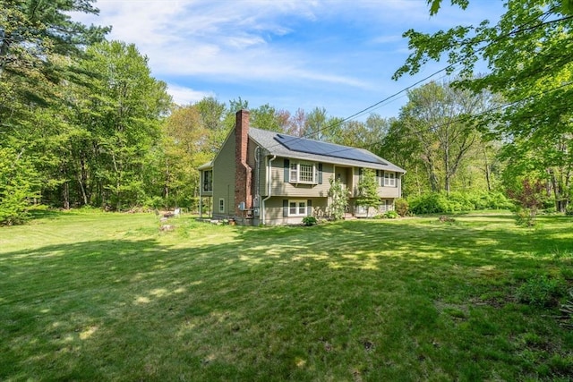 view of front of property featuring a chimney, solar panels, and a front lawn