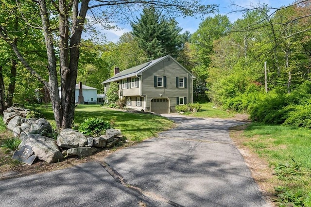 view of front facade with a chimney, asphalt driveway, an attached garage, and a front lawn