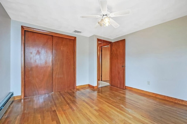 unfurnished bedroom featuring visible vents, a baseboard heating unit, wood finished floors, a closet, and baseboards