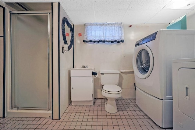 full bath with toilet, a stall shower, tile patterned flooring, a paneled ceiling, and washer / dryer