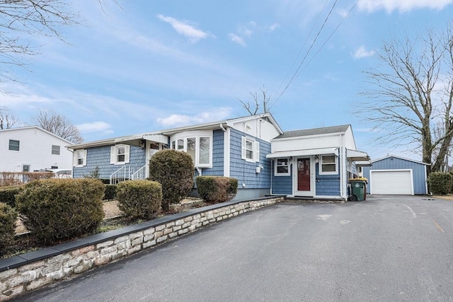 view of front facade featuring aphalt driveway, a detached garage, and an outbuilding