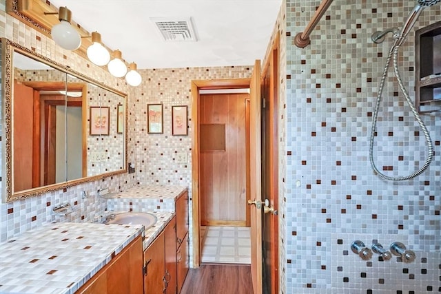 bathroom with a tile shower, visible vents, backsplash, and vanity