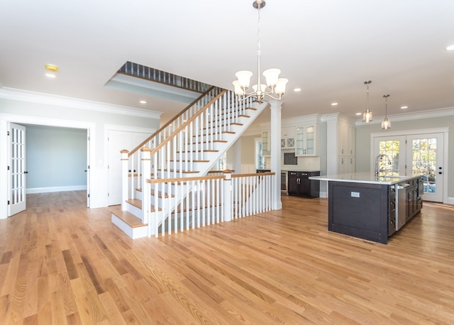 kitchen with pendant lighting, a center island with sink, crown molding, french doors, and light wood-type flooring