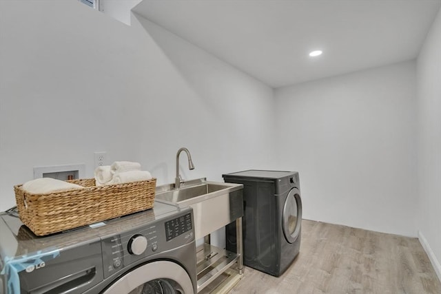 laundry area featuring washing machine and dryer, light hardwood / wood-style flooring, and sink