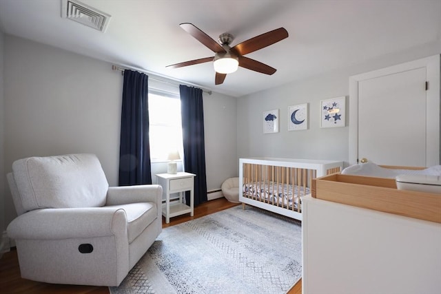 61 Colwell, Dedham, MA 02026 - bedroom featuring a crib, wood finished floors, a ceiling fan, and baseboard heating