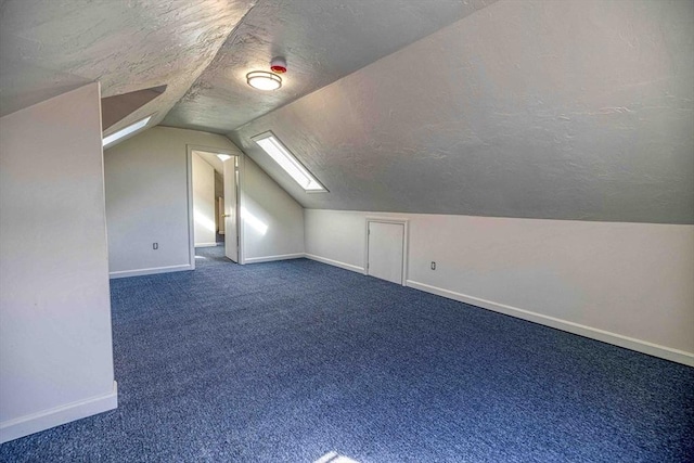 additional living space with vaulted ceiling with skylight, baseboards, dark colored carpet, and a textured ceiling