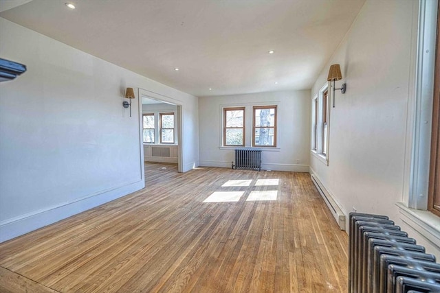 unfurnished living room with a baseboard heating unit, radiator, wood finished floors, and baseboards