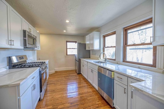 kitchen with light wood-style flooring, appliances with stainless steel finishes, white cabinets, a textured ceiling, and a sink