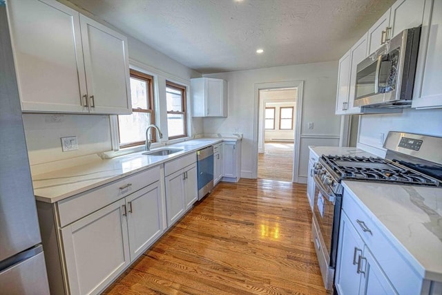 kitchen with stainless steel appliances, a healthy amount of sunlight, light wood-style flooring, and white cabinetry