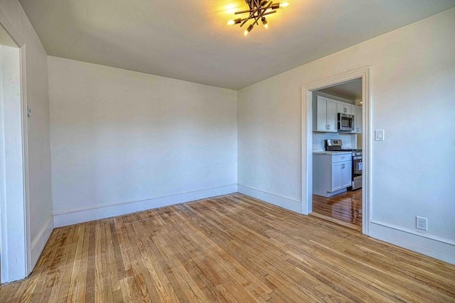 empty room with baseboards, light wood-type flooring, and a chandelier