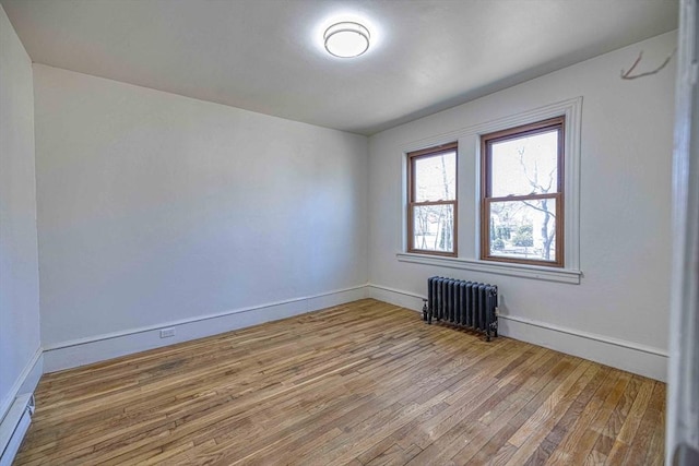 spare room with radiator, wood finished floors, and baseboards