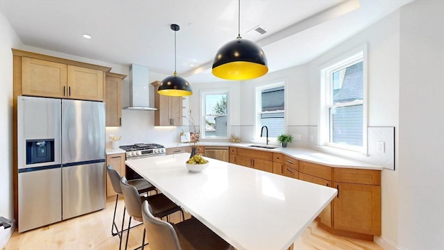 kitchen with appliances with stainless steel finishes, wall chimney range hood, a sink, light countertops, and recessed lighting