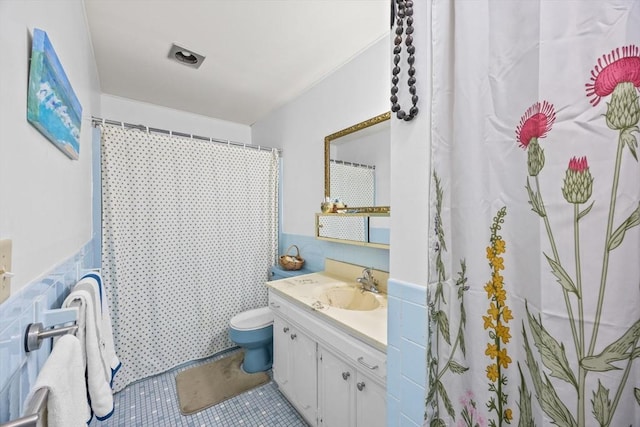 bathroom with tile walls, toilet, vanity, and tile patterned flooring