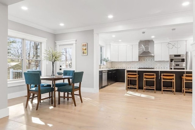 kitchen featuring white cabinets, light countertops, wall chimney range hood, backsplash, and modern cabinets