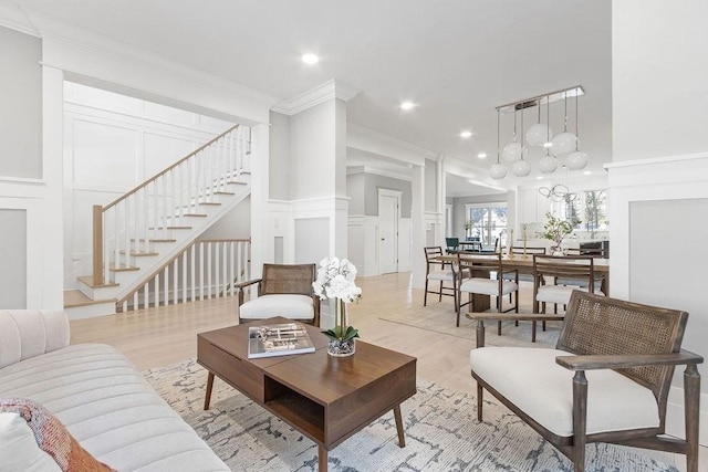 living area featuring wainscoting, ornamental molding, stairs, light wood-style floors, and a decorative wall